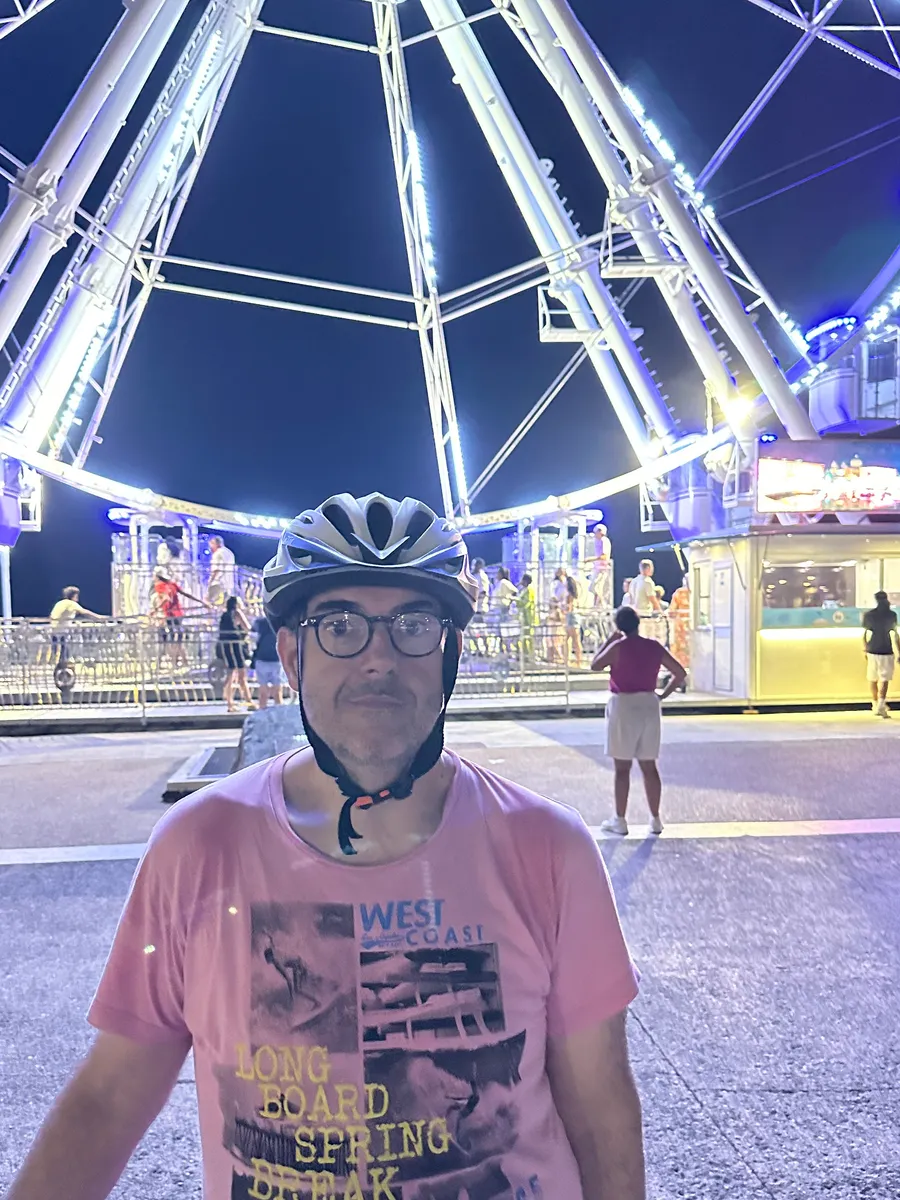 Ludo en casque de vélo, de nuit, devant une grande roue illuminée